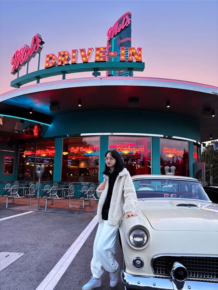 our-services-1 A model poses next to a vintage car at Mel's Drive-In diner during sunset.